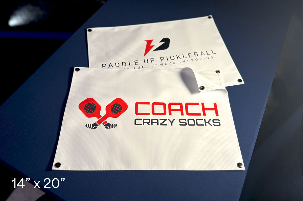 Custom pickleball net signs featuring Coach Crazy Socks and Paddle Up Pickleball logos, printed on 14x20 inch vinyl banners with grommets
