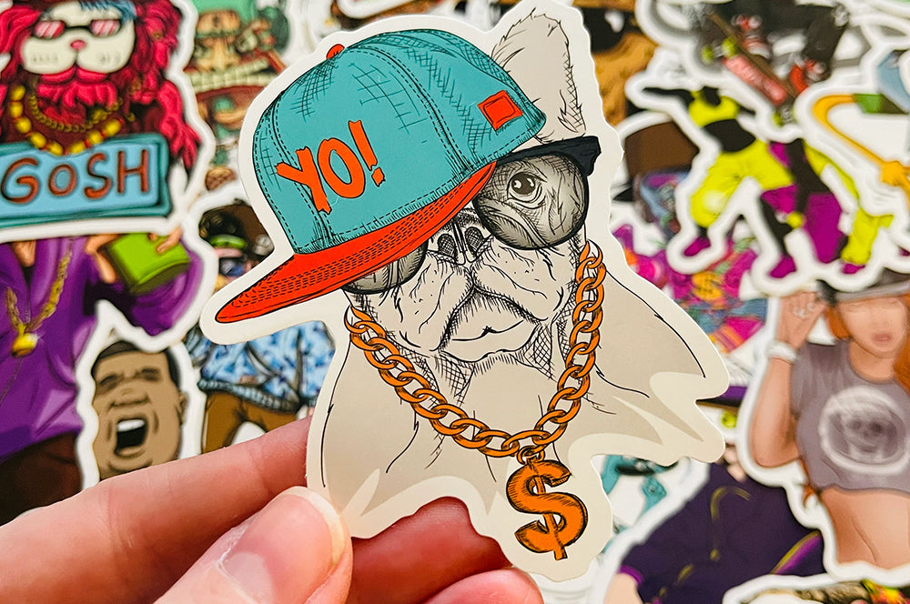 Illustrated die-cut sticker of a hip-hop-style bulldog wearing a hat and chain, held in hand.