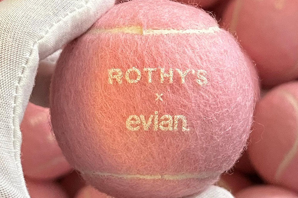 Pink custom tennis balls featuring Evian and Rothy’s collaboration branding.